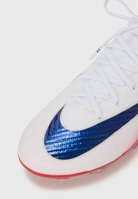 White sport shoe with a textured upper, featuring a blue swoosh design and red accents on the sole, complemented by white laces.