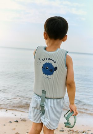 Stribet grå og blå børne svømmevest med et fiskemotiv. Barnet har stribede shorts på og holder grønne svømmebriller ved stranden.