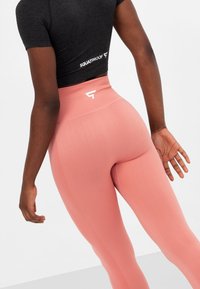 Leggings fucsia a vita alta con finitura texturizzata, dotate di un logo bianco sul retro e sulle cuciture laterali, abbinati a una maglietta nera aderente.