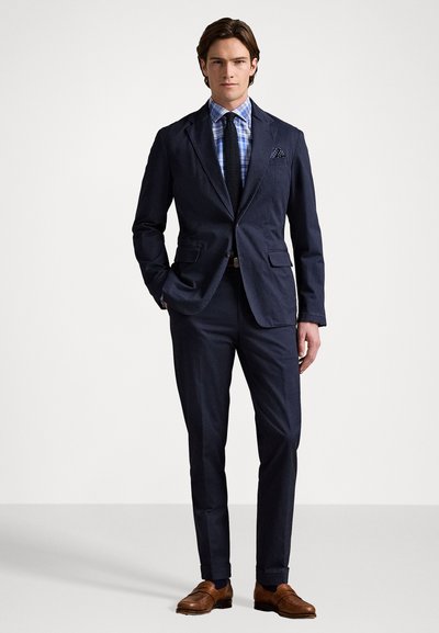 Navyblå kostym med slag, kombinerat med en ljusblå rutiga skjorta och svart slips. Texturerade bruna finskor fulländar outfiten.