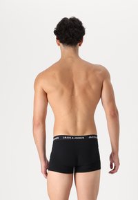 Schwarze Boxershorts mit einem elastischen Bund mit Logo, die eine enge Passform und eine glatte Textur bieten, von hinten auf einem nackten Oberkörper dargestellt.