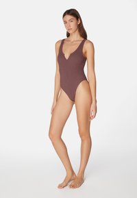 Geripptes Badeanzug-Einteiler in tiefem Mauve mit tiefem V-Ausschnitt und breiten Trägern, mit hoch geschnittenen Beinen und minimalistischer Gestaltung.