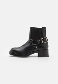 Black leather ankle boot with a rounded toe, elastic side panels, decorative strap with metal hardware, and a low block heel.