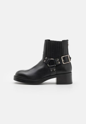 Black leather ankle boot with a rounded toe, elastic side panels, decorative strap with metal hardware, and a low block heel.