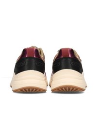 Une paire de baskets épaisses avec des semelles beige, des panneaux de talon noirs et des accents métalliques roses, vue de l'arrière sur fond blanc.