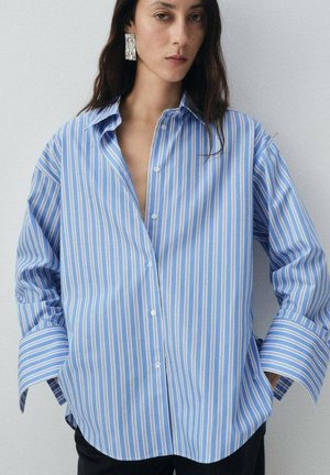 Camisa de botones a rayas azul y blanca con un corte holgado, que presenta mangas largas y un cuello puntiagudo. Tela de algodón suave, sin estampados.