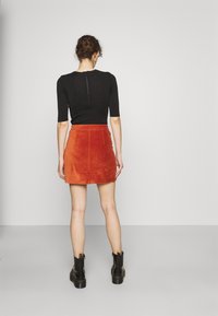 Haut noir à manches courtes avec une fermeture éclair au dos, associé à une mini-jupe en velours côtelé orange. Des bottines noires complètent la tenue.