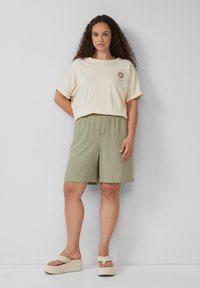 Crème, t-shirt met korte mouwen met een zon graphic; gecombineerd met lichtgroene, elastische shorts en beige platform sandalen.