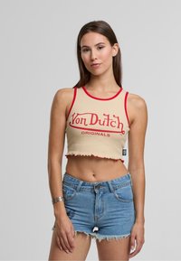 Béžový krátky top s červenými detailmi a na ňom v tučnom písme nápis "Von Dutch Originals". Má zúbkovaný lem. Nosený s modrými džínsovými šortkami.
