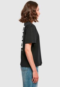 Tricou din bumbac negru cu maneci scurte, având un print grafic pe spate. Coconul este relaxat, cu o croială dreaptă și decolteu rotund.