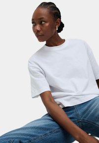 Weißes Baumwoll-T-Shirt mit Rundhalsausschnitt und kurzen Ärmeln, kombiniert mit blauen Jeans. Einfaches Design und lockere Passform.