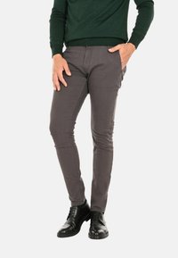 Pantaloni grigi slim-fit realizzati in misto cotone, con tasche laterali, abbinati a scarpe in pelle nera e a un maglione verde scuro.