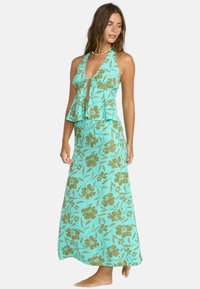 Aqua blomstermaxikjole med halterneck og lagdelt volangliv. Har gyldne blomsterinntrykk og en flytende silhuett.