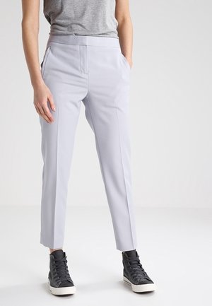 Pantalons taillés gris clair avec une coupe droite, des poches latérales et une texture lisse, assortis de baskets montantes noires.