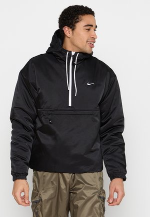 Schwarze Nylon-Pulloverjacke mit Kapuze, Zugbändern, einer vorderen Zip-Tasche und elastischen Bündchen. Mit einem kleinen weißen Logo auf der Brust.