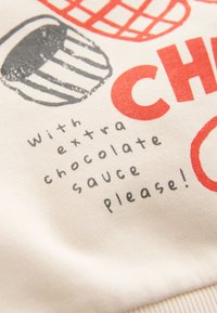 Auduma tuvplāns ar melniem un sarkaniem gardumu attēliem un rokraksta stilā uzrakstītu tekstu "with extra chocolate sauce please!".