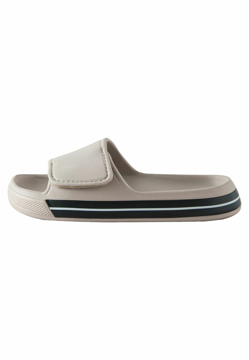 Helle beige Rutschsandalette mit einer strukturierten Oberfläche, einem breiten Riemen und einem schwarz-weißen gestreiften Akzent an der Sohle. Weiches Material, flaches Design.