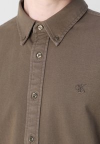 Braunes Hemd mit Knopfleiste, Knopfkragen und kleinem, auf der Brust gesticktem "cK"-Logo.