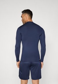 T-shirt atlético de manga longa azul-marinho com design ajustado; textura suave e decote redondo. Usado com calções azuis-marinho a condizer.