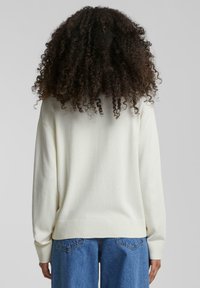 Pull crème clair avec un ourlet et des poignets côtelés, à la coupe décontractée et à la texture douce, porté avec un jean en denim bleu.
