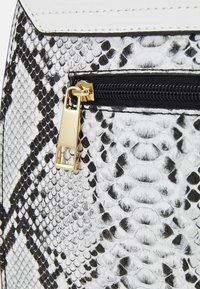 Faux cuir textured faux serpent noir et blanc avec une tirette dorée et des accents en cuir blanc contrastants. Présente un détail de poche zippée.