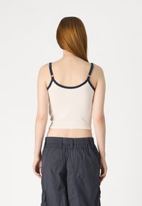 Krēmkrāsas pieguloša tank top ar tumši z blue akcentiem, regulējamām siksnām un gludu tekstūru. Saskaņota ar brīviem tumši pelēkiem cargo biksēm.