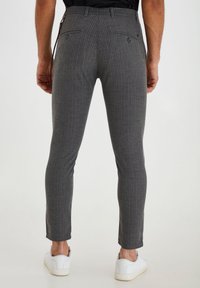Schmal geschnittene graue und blaue Nadelstreifen-Hosen mit Gesäßtaschen und glatter Textur, kombiniert mit weißen Sneakern.