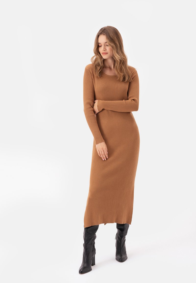 Długa, żebrowana sukienka w ciepłym brązowym kolorze, z długimi rękawami i dopasowanym krojem. Noszona z wysokimi, czarnymi botkami.