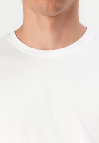 T-shirt en coton blanc avec un col rond, présentant une texture lisse et un design simple. Pas de motifs ni de graphiques visibles.