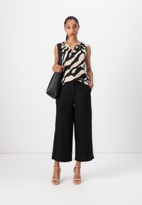 Ermeløs topp med zebra-mønster i beige og svart, kombinert med vide svarte bukser og lyse sandaler med stropper. Svart håndveske.