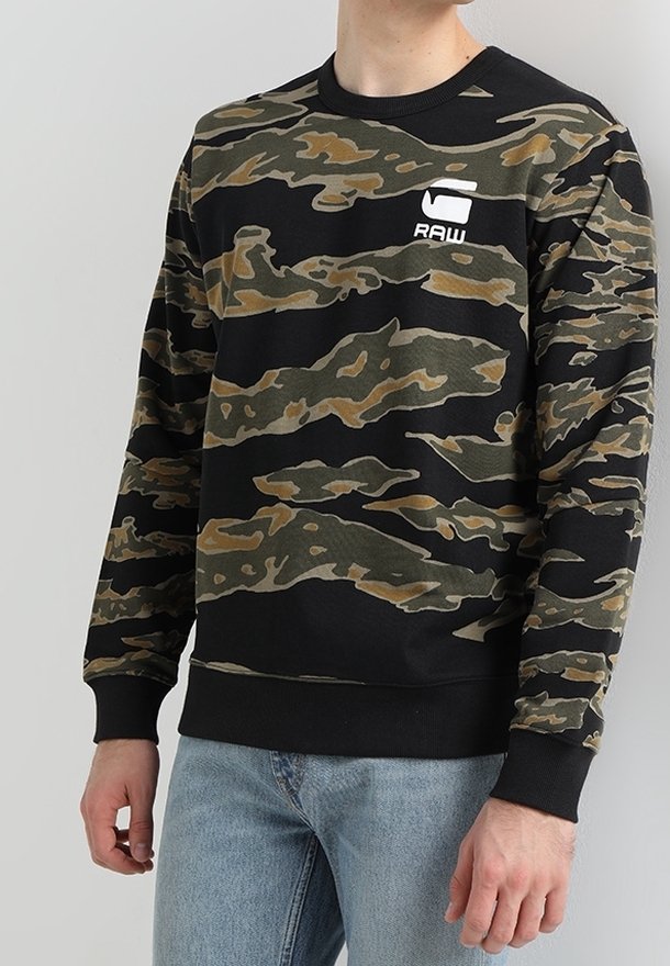 Kamouflagesweatshirt i svart, grön och beige. Har rundad halsringning, ribbade ärmslut och en vit logotyp på bröstet. Tillverkad av bomullsblandning.