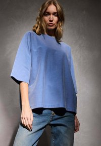 Haut bleu surdimensionné à manches courtes, fabriqué en tissu doux, avec une texture lisse et un ourlet droit, associé à un jean en denim clair.