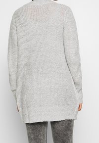 Lichtgrijze gebreide cardigan met een losse pasvorm, geribbelde kraag en lange mouwen met zijsneden voor extra bewegingsvrijheid. Geweven stof.