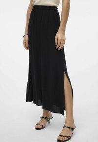 Gonna maxi nera con spacchi laterali, realizzata in tessuto leggero. Presenta una vita elasticizzata. Abbinata a sandali neri con lacci.