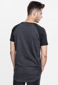 Men's t-shirt featuring a dark grey body with black raglan sleeves, made from a soft material, and a curved hemline at the back.
