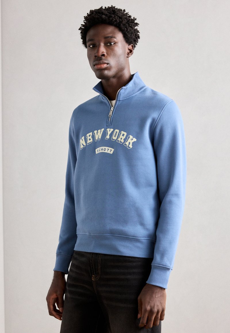 Svetle modrý sweatshirt s polovičním zipem, s žebrovanými rukávy a lemem, s potiskem "NEW YORK" a "SCHOTT" v krémové barvě. Hladký povrch, ležérní střih.