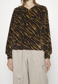 Chemise à manches longues rayée brun et noir, en forme de tigre, avec un col en V et une coupe décontractée, fabriquée en tissu doux. Associée à un pantalon cargo beige clair.