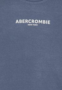 Sininen puuvillaneule, jossa on valkoinen teksti "ABERCROMBIE NEW YORK" rinnassa. Sileä rakenne ja pyöreä pääntie.