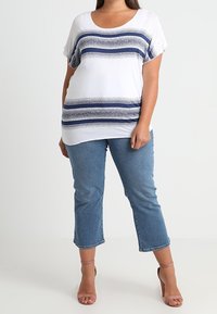 Top blanco con rayas horizontales azules; mangas cortas, escote redondeado. Jeans cortos de color azul claro. Tacones nude con tiras completan el look.