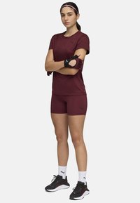 Maroon athletic t-shirt and shorts with black accents, paired with black gloves and sneakers featuring pink details. White socks visible.