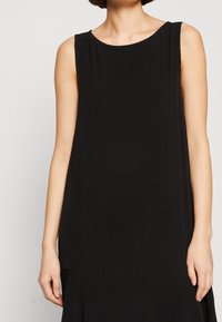 Robe noire sans manches avec un col rond, en tissu lisse, dotée d'une coupe ample et d'un ourlet légèrement arrondi.