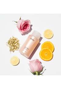 OUAI shampooflaska, opak rosa med ett vitt lock, omgiven av rosa rosor, jasminblommor, citron- och apelsinskivor på en vit bakgrund.