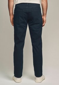 Jeans din denim albastru închis cu croi drept, două buzunare la spate, textură subtilă și talie. Asortați cu pantofi de culoare deschisă.