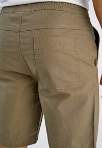 Szorty w kolorze khaki wykonane z teksturowanej tkaniny, z elastycznym pasem, bocznymi kieszeniami oraz pojedynczą tylną kieszenią z widocznymi detalami przeszyć.