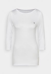 Camiseta blanca de manga larga con cuello redondo y un pequeño logo coloreado en el pecho, hecha de una tela suave y ligera.