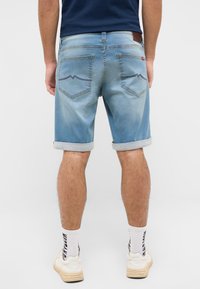 Jasnoniebieskie szorty dżinsowe z podwiniętymi nogawkami, z dwoma tylnymi kieszeniami i kontrastującymi detalami przeszyć. W połączeniu z białymi butami i prążkowanymi skarpetkami.