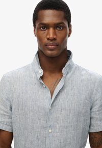 Camisa de manga corta, con cuello, en azul claro con sutiles rayas blancas. Tejido suave con cierre de botones y un corte holgado.