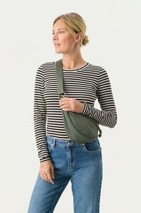 Borsa a tracolla verde realizzata in tessuto morbido; forma curva con una lunga tracolla, indossata a bandoliera e abbinata a una maglietta a righe bianche e nere.