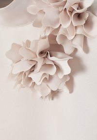 Světle růžová blůza s látkovými květinovými aplikacemi v vrstveném designu. Hladká textura s kulatým výstřihem a jemnými švy.