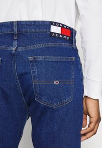 Jeans in denim blu scuro con una finitura testurizzata, dotati di un patch con il logo TOMMY JEANS e un piccolo accento del logo sulla tasca posteriore.